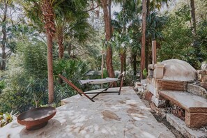 A view of the fire pit, hammock and wood oven in lush surrounds. 
