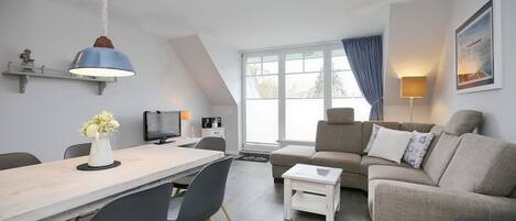 Wohnzimmer mit Sofaecke, TV, Esstisch und Blick zum Balkon