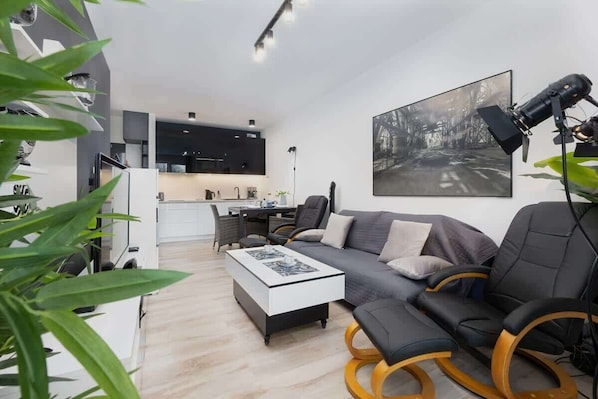 A modern living room with a sectional gray sofa, a sleek white coffee table, and contemporary decor. The space has a minimalist and clean design with soft, ambient lighting.