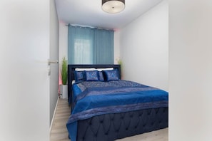 A cozy bedroom with a blue theme, featuring a bed with blue bedding and a matching headboard. The room is bright and minimal, with simple decor and a calming color palette.