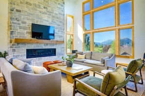 Experience the cozy living room, outfitted with plush seating, a fireplace, an expansive smart TV, and large windows that frame the breathtaking mountain vistas.