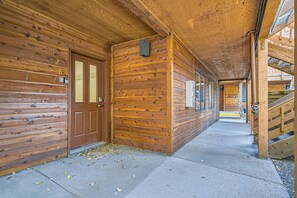 A wooden exterior hallway with a brown door labeled "28," adjacent windows, and stairs leading to an upper level. Leaves are scattered on the concrete walkway.