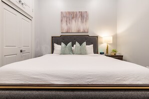 Side 1: Spacious guest bedroom with a king bed and designer built-in closet. Includes a nightstand, lamp, hangers, luggage rack, alarm clock, white noise machine, and a 50'' Samsung Smart 4K TV with streaming and DIRECTV Entertainment.