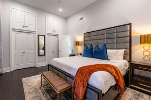 Side 1: Spacious primary bedroom with king bed, ensuite bath, and designer built-in closets. Includes black-out curtains, hangers, luggage racks, white noise machine, and a 43" Samsung Smart 4K TV with streaming and DIRECTV Entertainment.