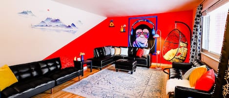 A spacious living room with a striking red and white wall, adorned with a money tapestry, and furnished with a sleek black couch, creating a bold and inviting space.