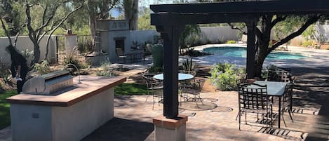 Outdoor dining under wooden pergola and olive tree near bar and grill 