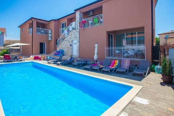 La façade de la maison, l'espace piscine avec chaises longues à usage commun