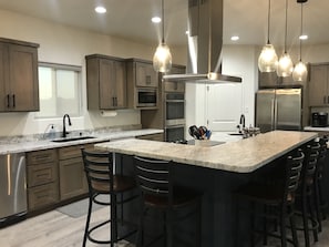 Kitchen island with stovetop, range hood, fridge, and bar with pendant lights