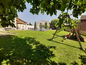 Vue du fond du jardin avec balançoire et cabane pour enfant sur pilotis