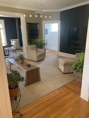 View of the living room from the kitchen. An 82" TV is on the dark wall. 