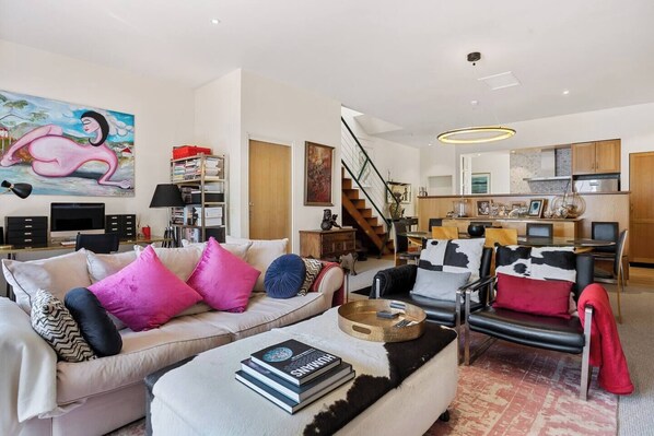 Bask in the vibrant atmosphere of the spacious living room, featuring retro furnishings, a comfortable sofa, leather armchairs, and a TV—perfect for relaxing after a day exploring Hobart.

