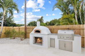 Outdoor pizza oven w/ built-in Coyote grill and granite countertops.