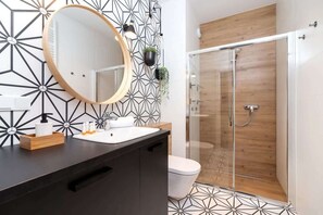 A stylish bathroom with geometric-patterned tiles, a round mirror, and a walk-in shower with glass doors.