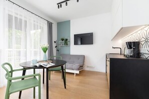 A bright dining area with a glass-top table and green chairs, situated near large windows for ample natural light.