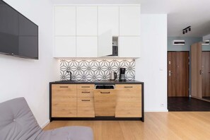 A compact, modern kitchen with white cabinets, wooden lower drawers, and a black backsplash featuring patterned tiles.