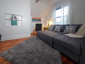 The living room includes a SMART TV, books, and a convertible couch bed.