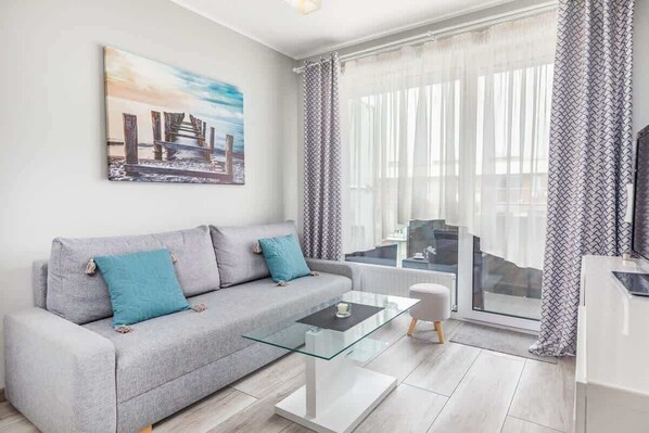 A bright living room with a gray sofa, decorative pillows, and a glass coffee table in front.