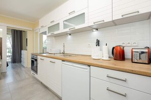 A sleek kitchenette with white cabinetry, a wooden countertop, and modern appliances, arranged in a practical layout.