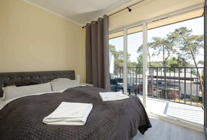 A cozy bedroom featuring a neatly made queen-sized bed with dark gray bedding, soft lighting, and large windows.