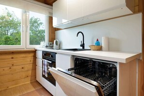 A compact yet modern kitchenette with wooden cabinetry, white countertops, and essential appliances, blending functionality with natural aesthetics.
