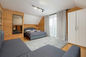 A bedroom with wooden paneling, a double bed, and a large window covered with curtains, offering a rustic and peaceful vibe.