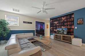 Cozy lounge with faux library wall, sleek sectional, and connected theater room.
