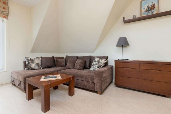 A cozy living room with a slanted ceiling, featuring a gray sofa, wooden coffee table, and a decorative floor lamp.