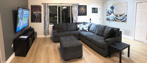 Large living area with sectional couch ottoman and 70” TV.  