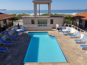 Área da piscina cercada com espreguiçadeiras, mesas, cadeiras e guarda-sol