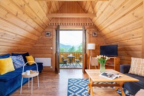 A cozy living space with sloped wooden ceilings, a blue sofa, and yellow accent pillows, complemented by a wooden coffee table and rustic decor.