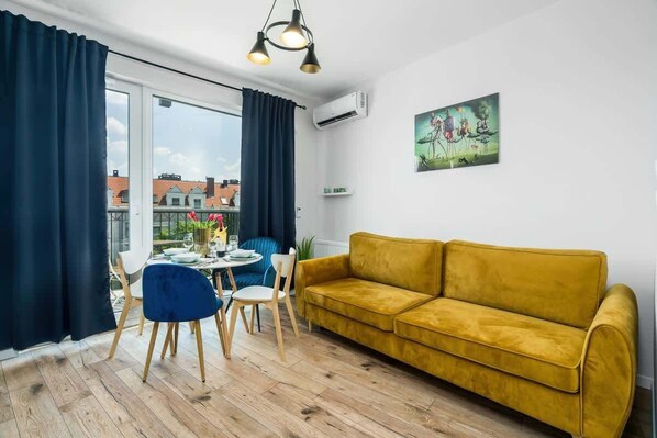 A stylish living room with a yellow sofa. The space is well-lit by natural light streaming through large windows with navy curtains.
