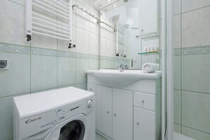 A clean, tiled bathroom featuring a sink, bathtub, and washing machine, ensuring comfort and functionality for longer stays.