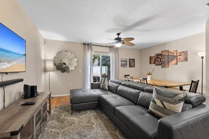 Main living room with patio access. Showing sectional, TV, ceiling fan and dining table