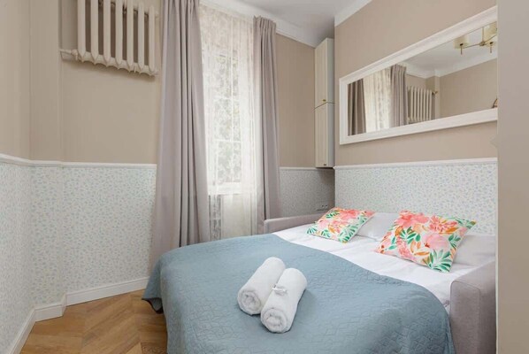 A stylish bedroom featuring a large window, light furniture, and vibrant decor for a relaxing atmosphere.