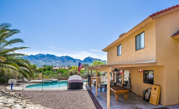 Backyard mountain view of pool, spa, pool table, and corn hole game.