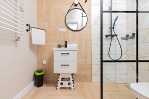  A compact bathroom with a glass-walled shower, a round mirror, and beige tiled walls.