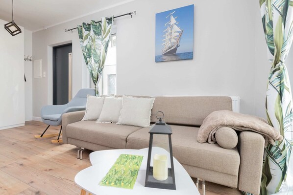 A bright living room with a light beige sofa, a coffee table, and a colorful wall painting above the couch. The decor is minimalist with natural light streaming in.