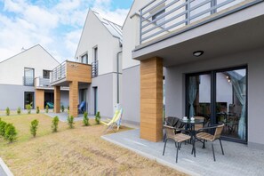 A modern housing complex with light-colored walls, wooden elements, and a neatly arranged parking area in front.