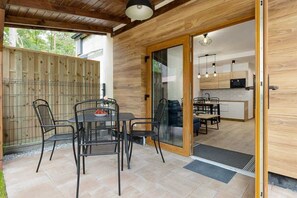 A charming outdoor patio space with a round metal table and chairs, surrounded by greenery. The table is set for an outdoor meal, making it a perfect spot for relaxing in the fresh air.