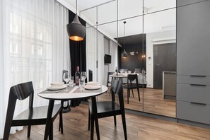 A cozy dining space with a small table and chairs next to a modern kitchen. The kitchen is equipped with sleek gray cabinets and stainless steel appliances.