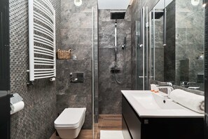 A stylish bathroom featuring a walk-in shower with glass doors, sleek black and gray tiles, and modern fixtures.
