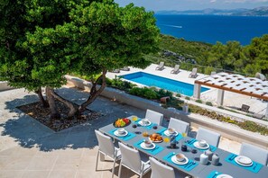 A luxurious outdoor terrace with a dining table and chairs and comfortable deckchairs by the heated swimming pool