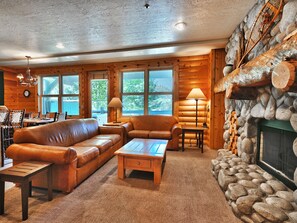 A cozy living room with two leather sofas and a river stone fireplace wall with log mantlepiece.