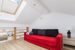 A simple yet vibrant living area featuring a red sofa against a wooden wall, beneath a slanted ceiling.