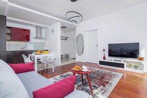 Another view of the living room, showcasing the dining area with chairs and a table. The bright space is complemented by vibrant wall art and a large window.