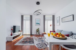 The dining and living space combined, highlighting the dining table with a fruit bowl centerpiece, large windows, and wooden flooring.