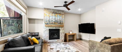 Living area offering large windows with great light, gas fireplace, hardwood flooring with radiant heating, large flatscreen HD TV, and a queen sleeper sofa.