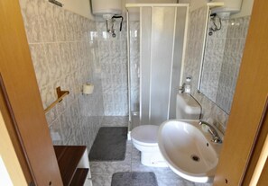 The bathroom has a shower, sink with mirror, cabinet and toilet.