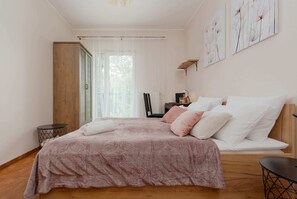 A bedroom featuring soft pink bedding, decorative pillows, and a side table with a lamp, offering a warm and inviting space.