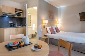 A neatly arranged room featuring a small dining area, cozy bedding, and a glimpse of an adjacent bathroom.